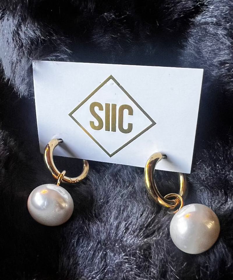 Pearl earrings on a card with 'SIC' logo against a dark fur background