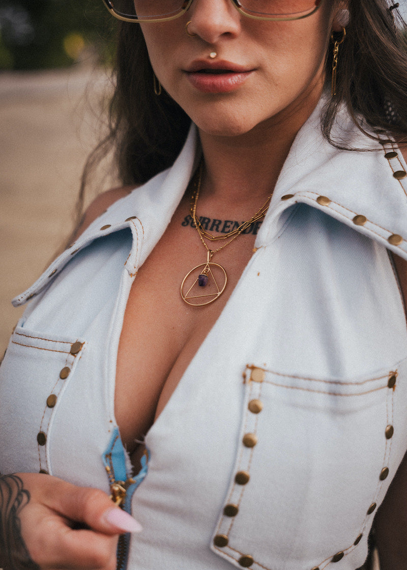 Close-up of a person wearing a light blue denim jacket with gold buttons, gold necklace, and sunglasses wearing soul sister since 1969.