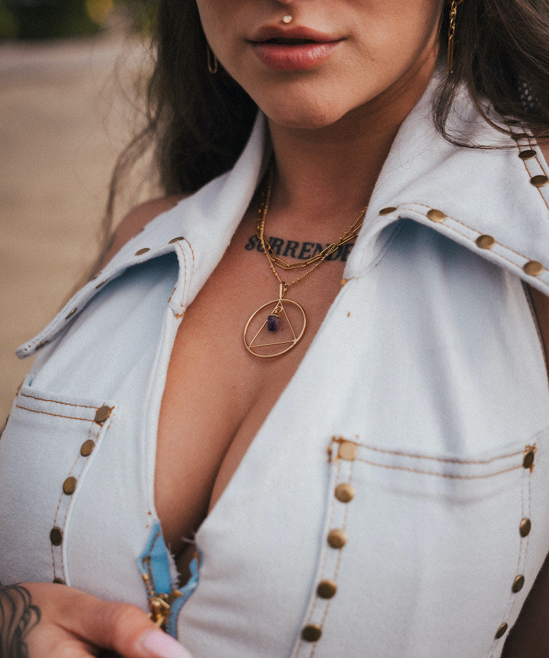 Close-up of a person wearing a light blue denim jacket with gold buttons, gold necklace, and sunglasses wearing soul sister since 1969.