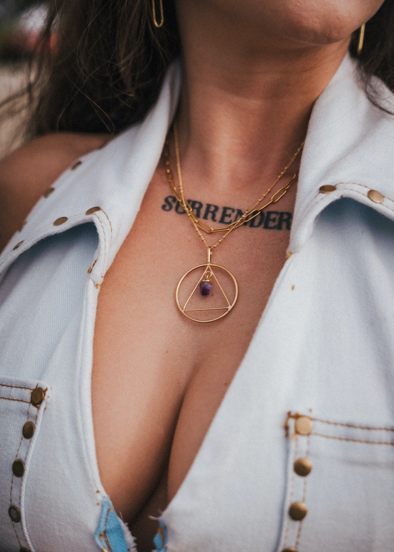 Close-up of a person wearing a gold necklace with a pendant, showing a tattoo on the neck wearing Soul Sister since 1969.