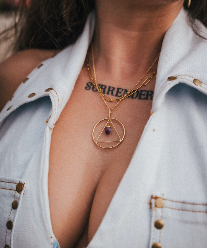 Close-up of a person wearing a gold necklace with a pendant, showing a tattoo on the neck wearing Soul Sister since 1969.