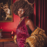 Woman in a red sequin studio 54 style disco jumpsuit with 70s style fur holding a cocktail in a dimly lit room.