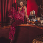 70s babe in a sparkly red jumpsuit sitting at a bar with a red curtain background retro setting