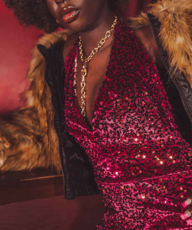 Disco babe wearing a red sequin jumpsuit with a  1970 retro inspired fur coat against a red background