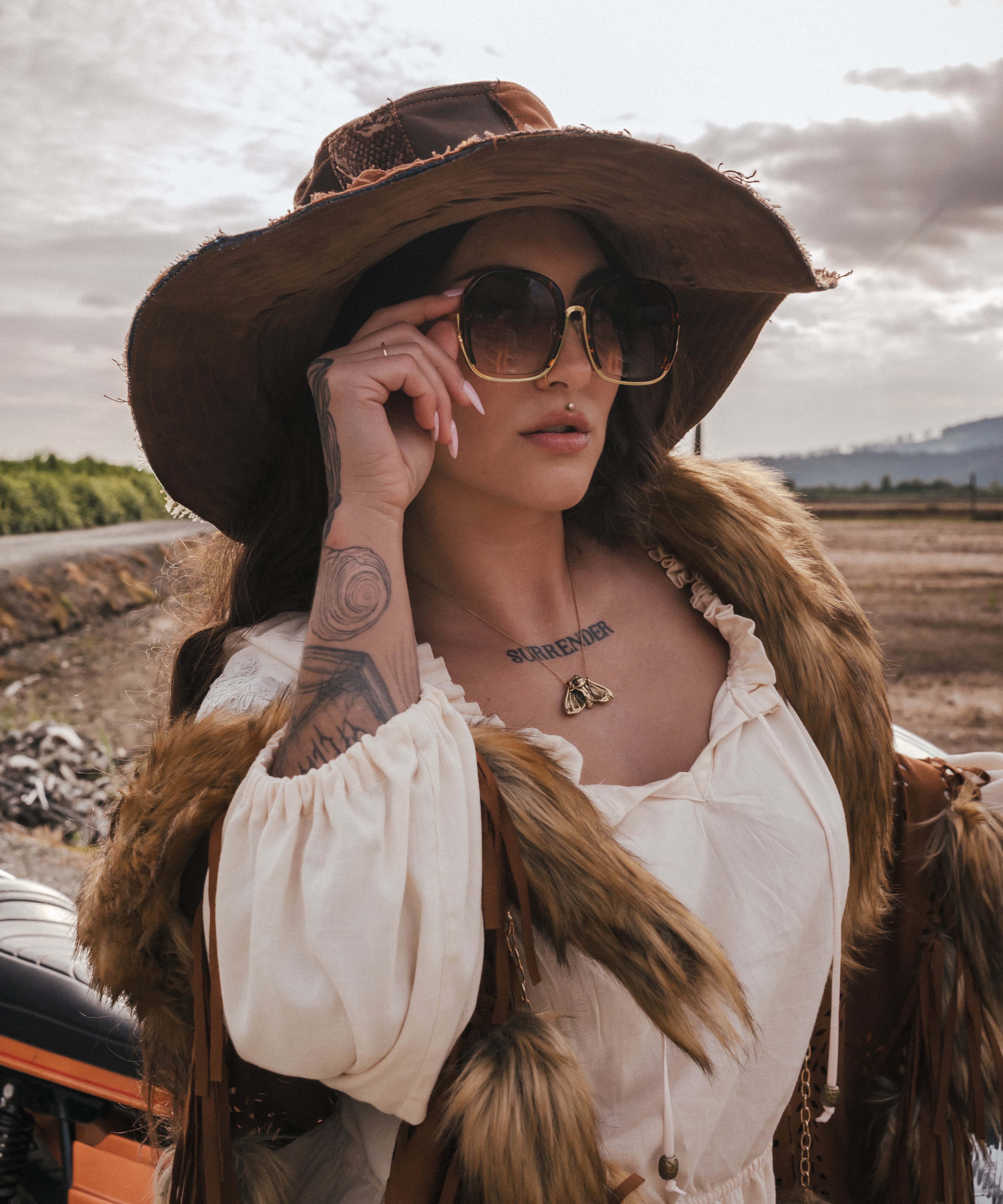 Woman in a white dress and brown hat with sunglasses, standing outdoors. wearing soul sister since 1969