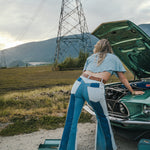 Person in blue and white outfit working on a green car in an open field with power lines in the background Wearing Soul Sister since 1969. .
