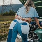 Person wearing blue jeans and a light blue top standing next to an open car hood outdoors Wearing Soul Sister since 1969. .