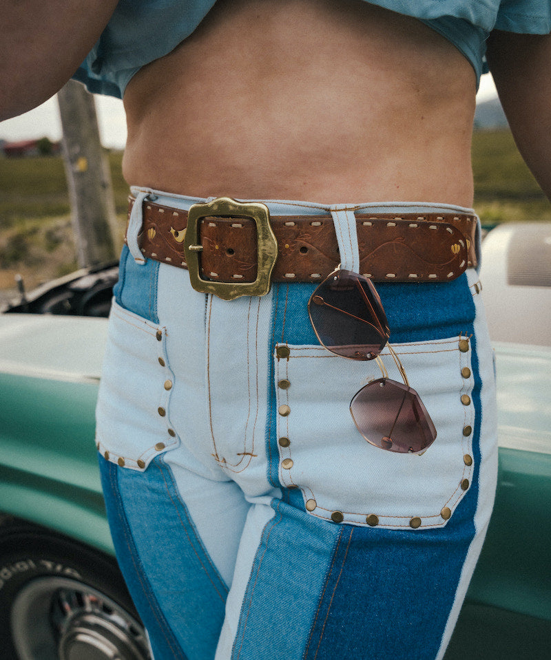 Person wearing a blue shirt and white pants with a brown belt and sunglasses, standing next to a vintage car Wearing Soul Sister since 1969. 
