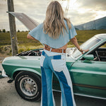 Person wearing a blue outfit standing next to a vintage car with mountains in the background Wearing Soul Sister since 1969. 