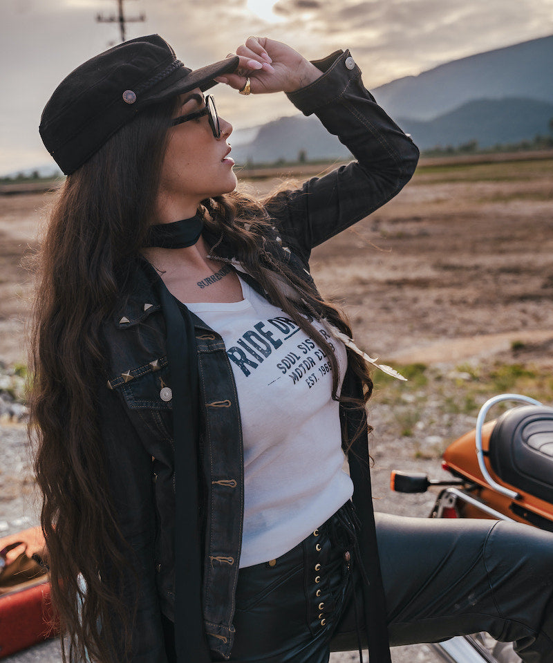 Woman with long hair and a hat standing outdoors with mountains in the background wearing Soul Sister since 1969.