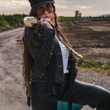 Woman in a black jacket and hat holding a bottle in an open field wearing Soul Sister since 1969.