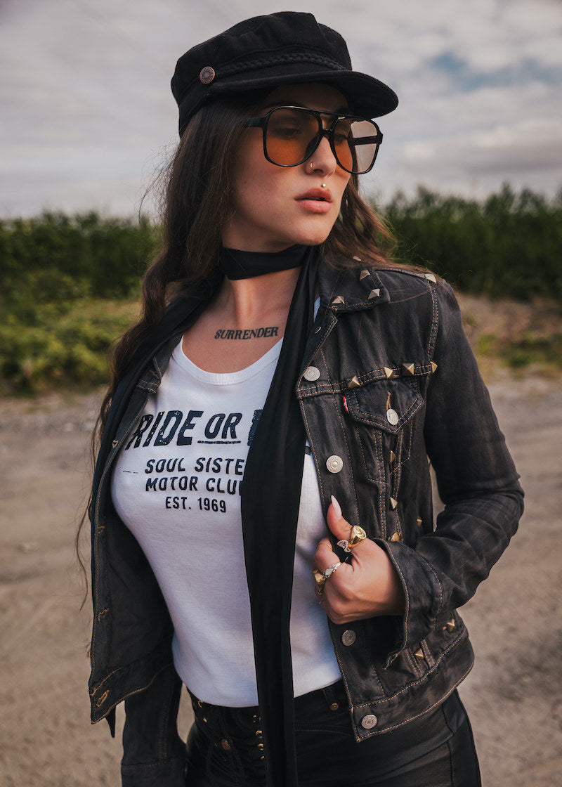 Woman wearing a black jacket, white t-shirt, and sunglasses outdoors wearing Soul Sister since 1969.