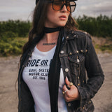 Woman wearing a black jacket, white t-shirt, and sunglasses outdoors wearing Soul Sister since 1969.