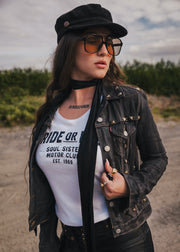 Woman wearing a black jacket, white t-shirt, and sunglasses  and a black hat outdoors wearing Soul Sister since 1969.