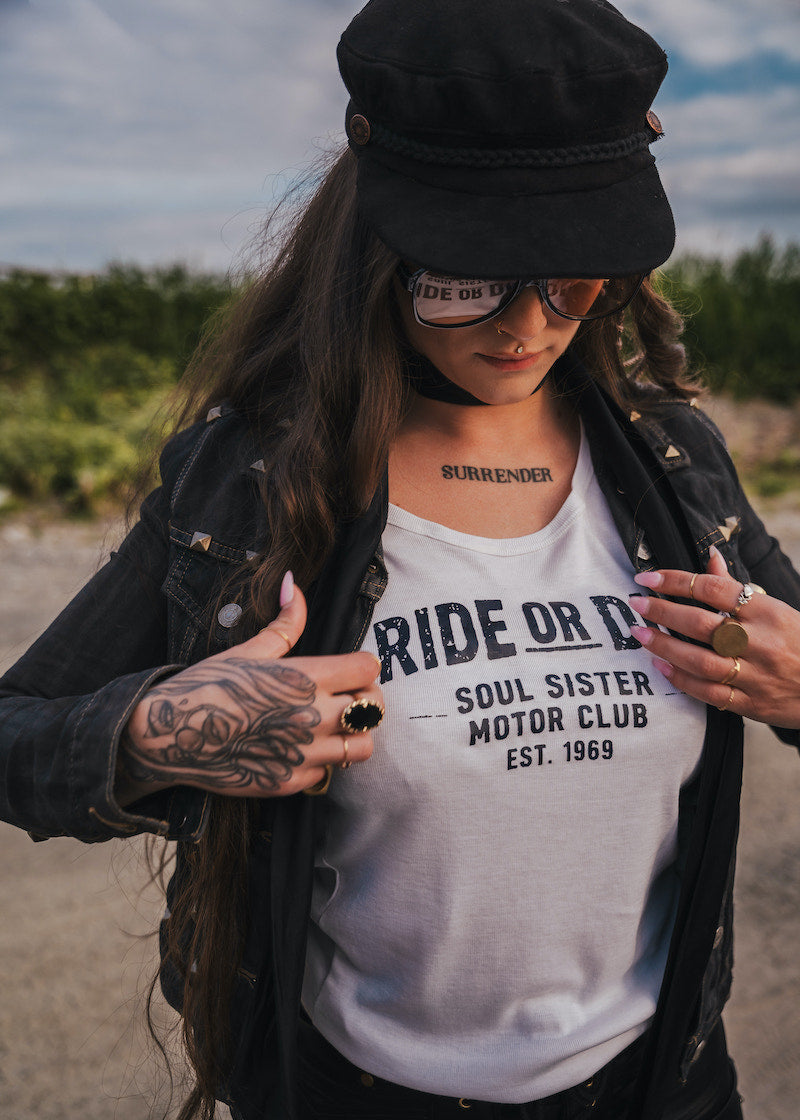Person wearing a white t-shirt with text, black jacket, and cap outdoors wearing Soul Sister since 1969.