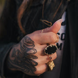 Hand with tattoos and multiple rings, wearing a dark jacket wearing clothing designed and made by Soul Sister since 1969..