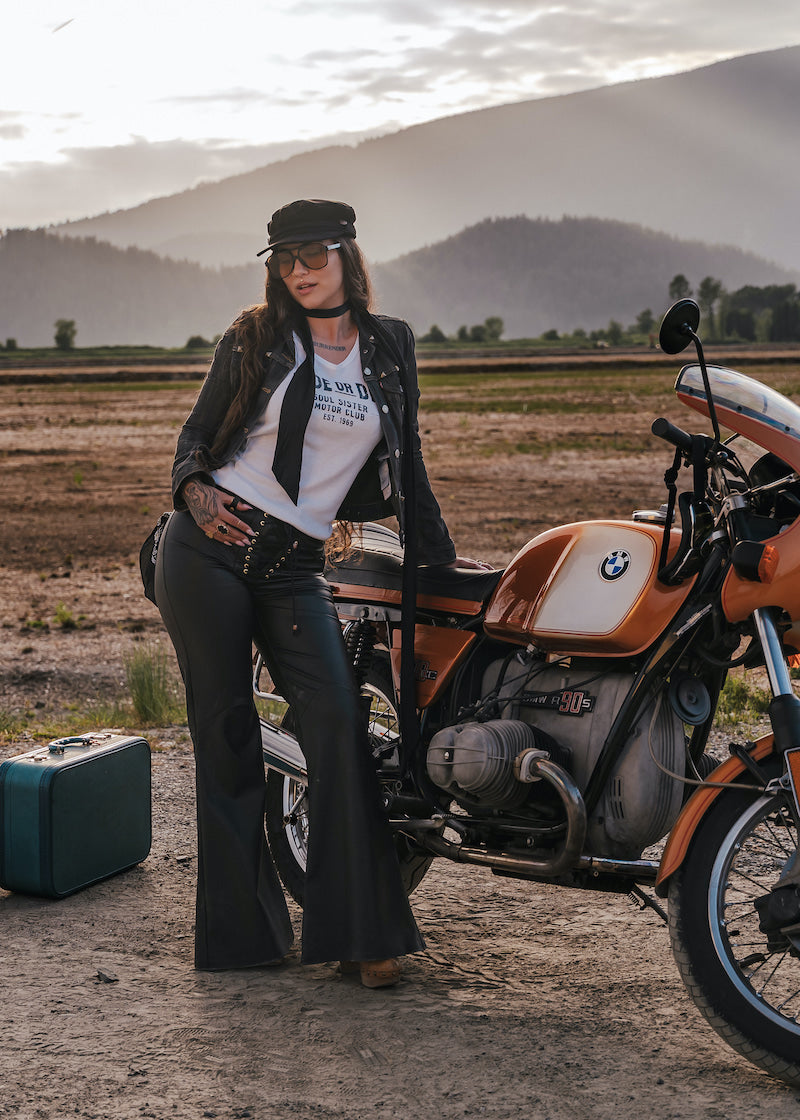 Woman standing next to a motorcycle in a desert landscape with mountains in the background wearing Soul Sister since 1969