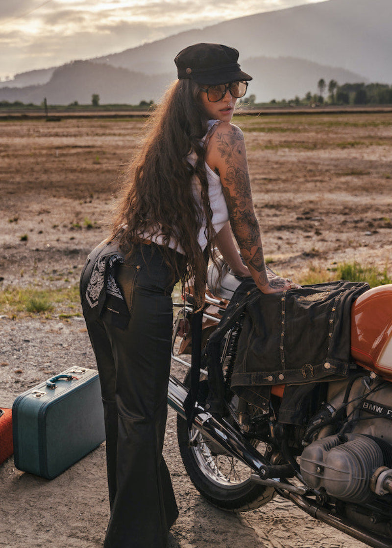 Person with tattoos standing next to a motorcycle in a desert landscape with mountains in the background wearing Soul Sister since 1969