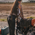 Person with tattoos standing next to a motorcycle in a desert landscape with mountains in the background wearing Soul Sister since 1969