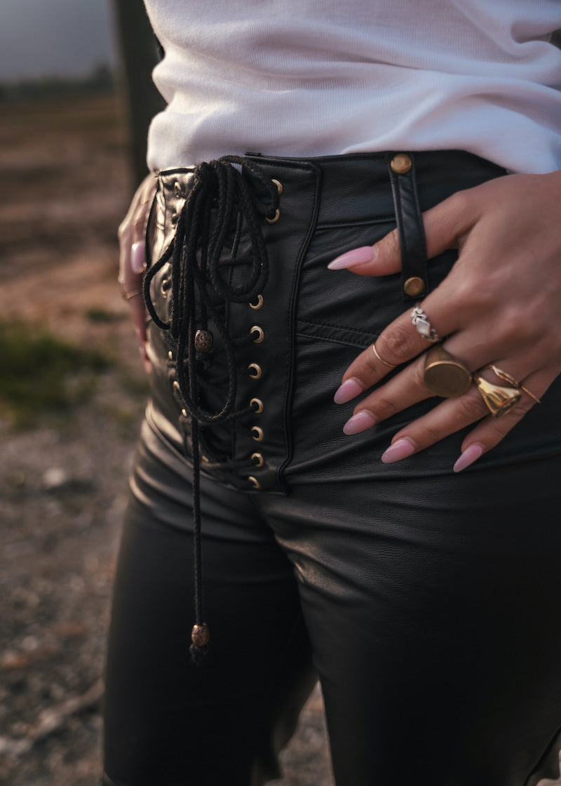 Person wearing a black lace-up vegan leather Bell bottom jeans with gold accents and a white top designed and made by Soul Sister since 1969.