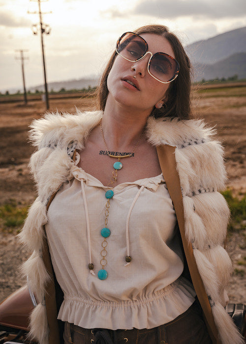Woman wearing sunglasses and a fur vest in a desert landscape wearing soul sister since 1969