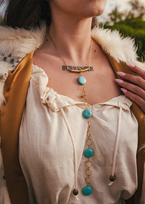 Person wearing a necklace with turquoise stones and a tattoo on their chest wearing soul sister since 1969.
