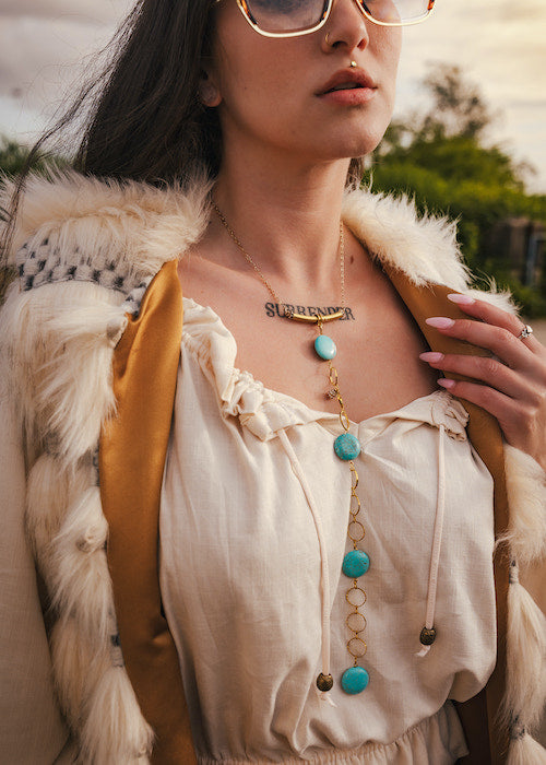 Person wearing a white blouse with turquoise beads and gold necklace, outdoors. wearing soul sister since 1969