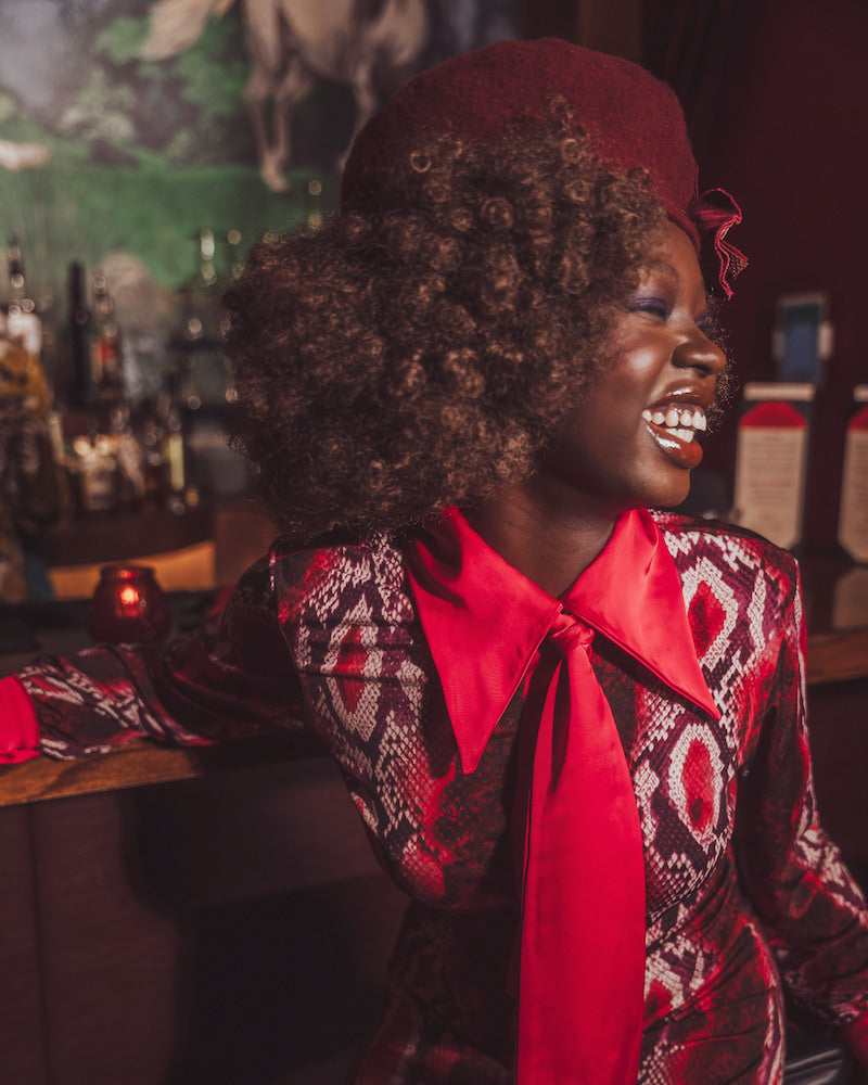 Woman in a stylish outfit with a red scarf and patterned jacket in a bar setting