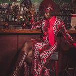 A woman sits at the bar with a martini in her hand in a speakeasy setting wearing a cool 70s inspired retro dress in snake print