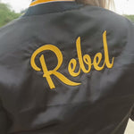 model wears satin bomber jacket with the words Rebel on the back
