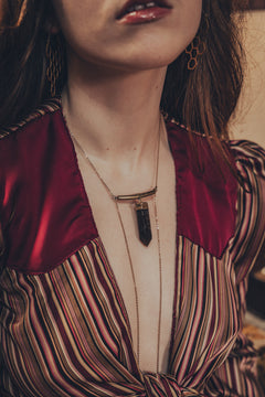 A close-up image of a person wearing a red and striped shirt, showcasing a gold plunging necklace with a smoky quartz stone designed by soul sister since 1969