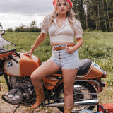 Woman sitting on a motorcycle in a field with a suitcase nearby wearing Soul Sister since 1969