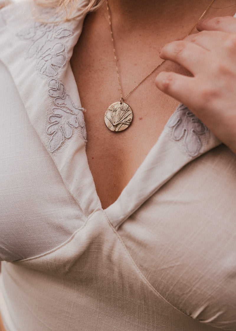 Close-up of a person wearing a gold necklace with a circular pendant. wearing Soul Sister since 1969
