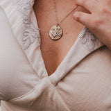Close-up of a person wearing a gold necklace with a circular pendant. wearing Soul Sister since 1969
