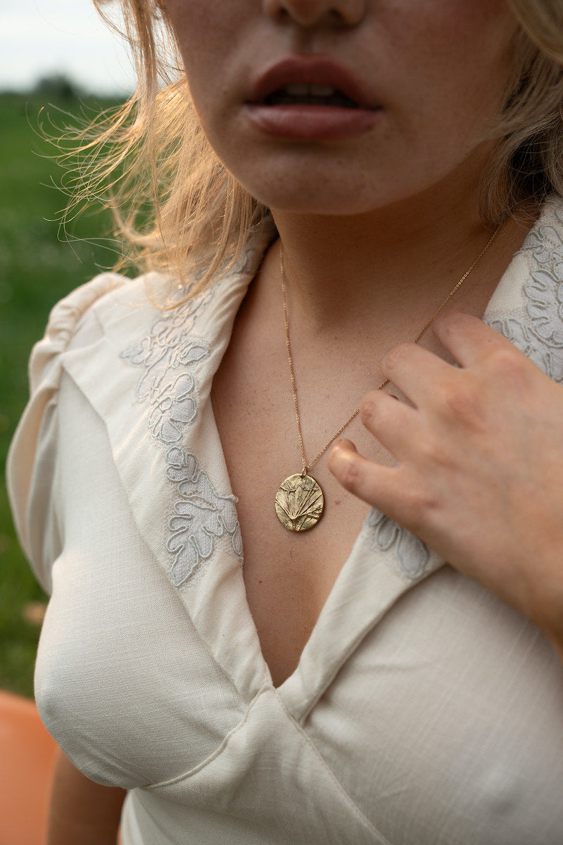 Close-up of a person wearing a gold necklace with a pendant outdoors wearing Soul Sister since 1969