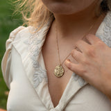 Close-up of a person wearing a gold necklace with a pendant outdoors wearing Soul Sister since 1969