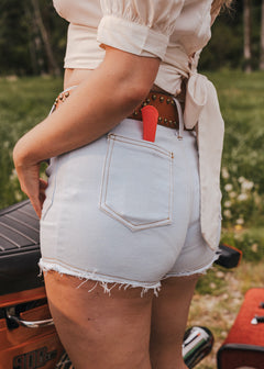 Person wearing light blue denim shorts with a red tool in the pocket, standing outdoors wearing Soul Sister since 1969.