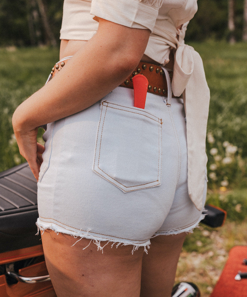 Person wearing light blue denim shorts with a red tool in the pocket, standing outdoors wearing Soul Sister since 1969.