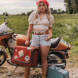 Woman standing next to a motorcycle with a suitcase in a field wearing Soul Sister since 1969
