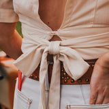 Person wearing a beige wrap top with a brown belt and light blue jeans by Soul Sister since 1969