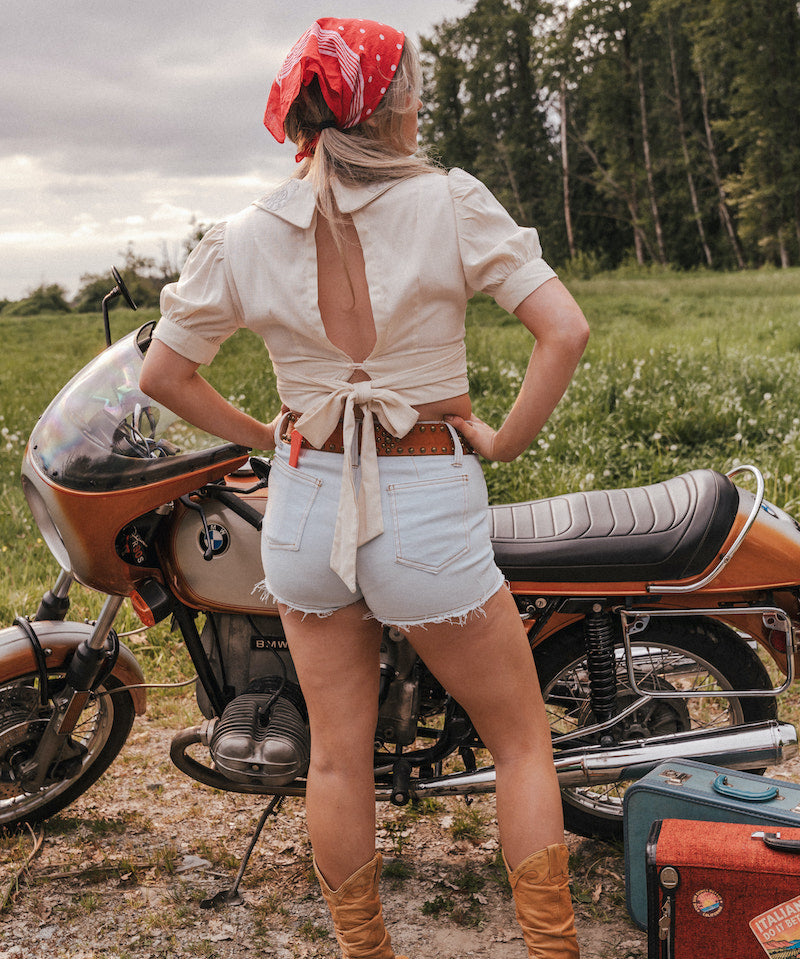 Person standing next to a motorcycle in a field with a red bandana and open back top wearing Soul Sister since 1969..